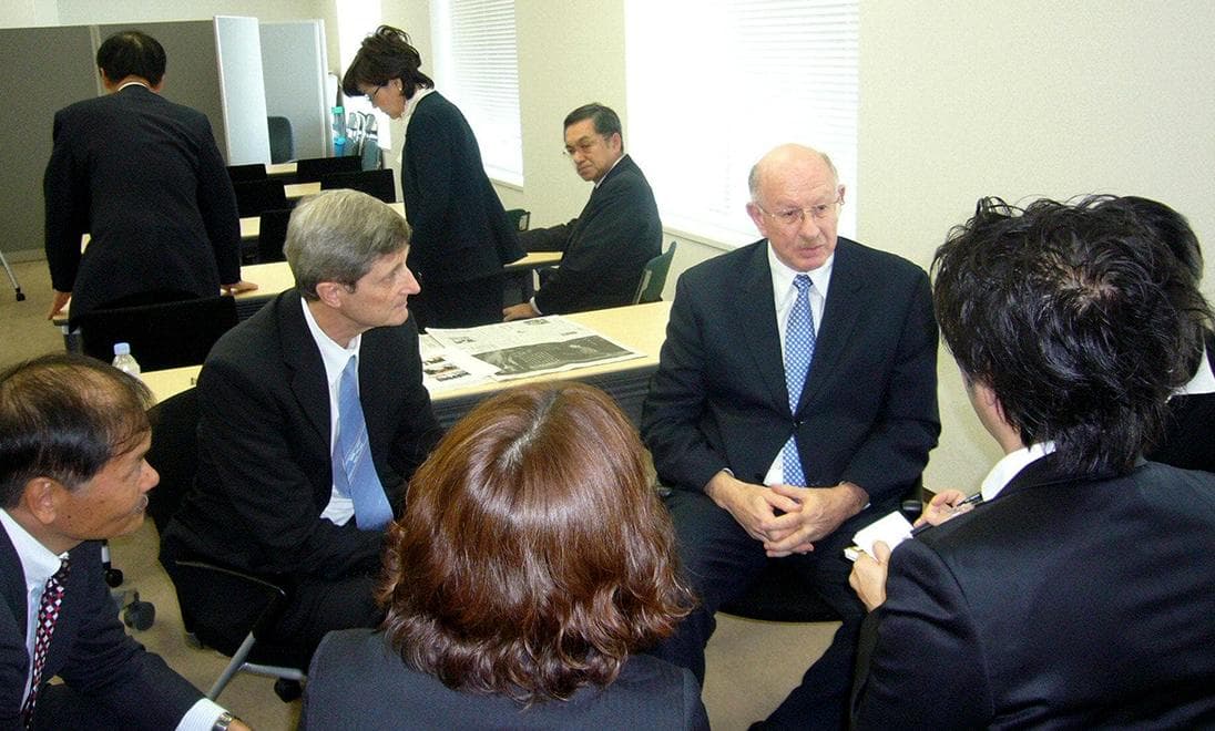 Several men and women in suits in a small white meeting room.