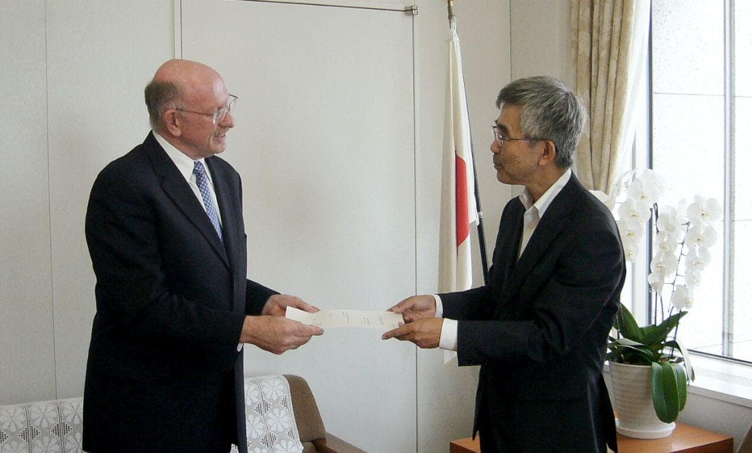 President Dorfan in a meeting room, receiving a white certificate from a Japanese official.