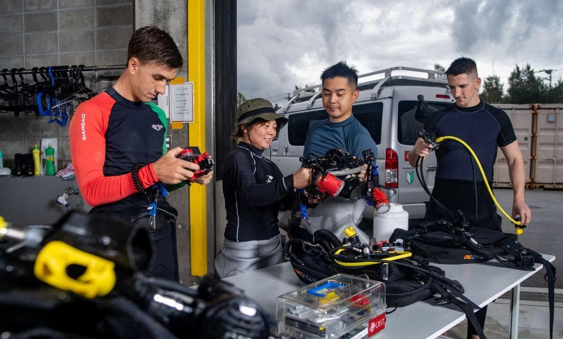 Four divers cleaning and inspecting equipment on a table.